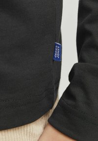 Must have mustakastane helesiga "JACK & JONES" sildiga, mis on nähtav külgõmblusel, tuues esile materjali ja õmbluste detaile.