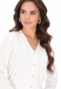 Fehér kardigán puha anyagból, V-nyakkivágással, hosszú ujjakkal és öt gyöngyszerű gombbal elöl.