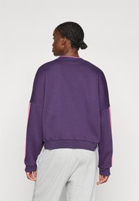 Sudadera morada de corte relajado, con mangas largas y detalles en rosa en los laterales. El material parece suave con puños acanalados.