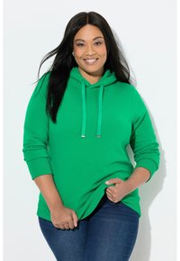 Zelená mikina s kapucí z měkkého materiálu, s přední kapsou, stahovací kapucí a žebrovanými manžetami. Kombinováno s tmavými džínami.