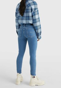 Camisa de franela a cuadros azul recortada y jeans ajustados de color azul claro. Botas gruesas blancas con un acabado texturizado. Bolsillos traseros visibles en los jeans.