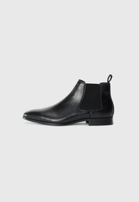 Botas de tobillo de cuero negro con paneles elásticos en los lados, puntera afilada y un pequeño tacón. Presenta una lengüeta en la parte posterior para facilitar su uso.