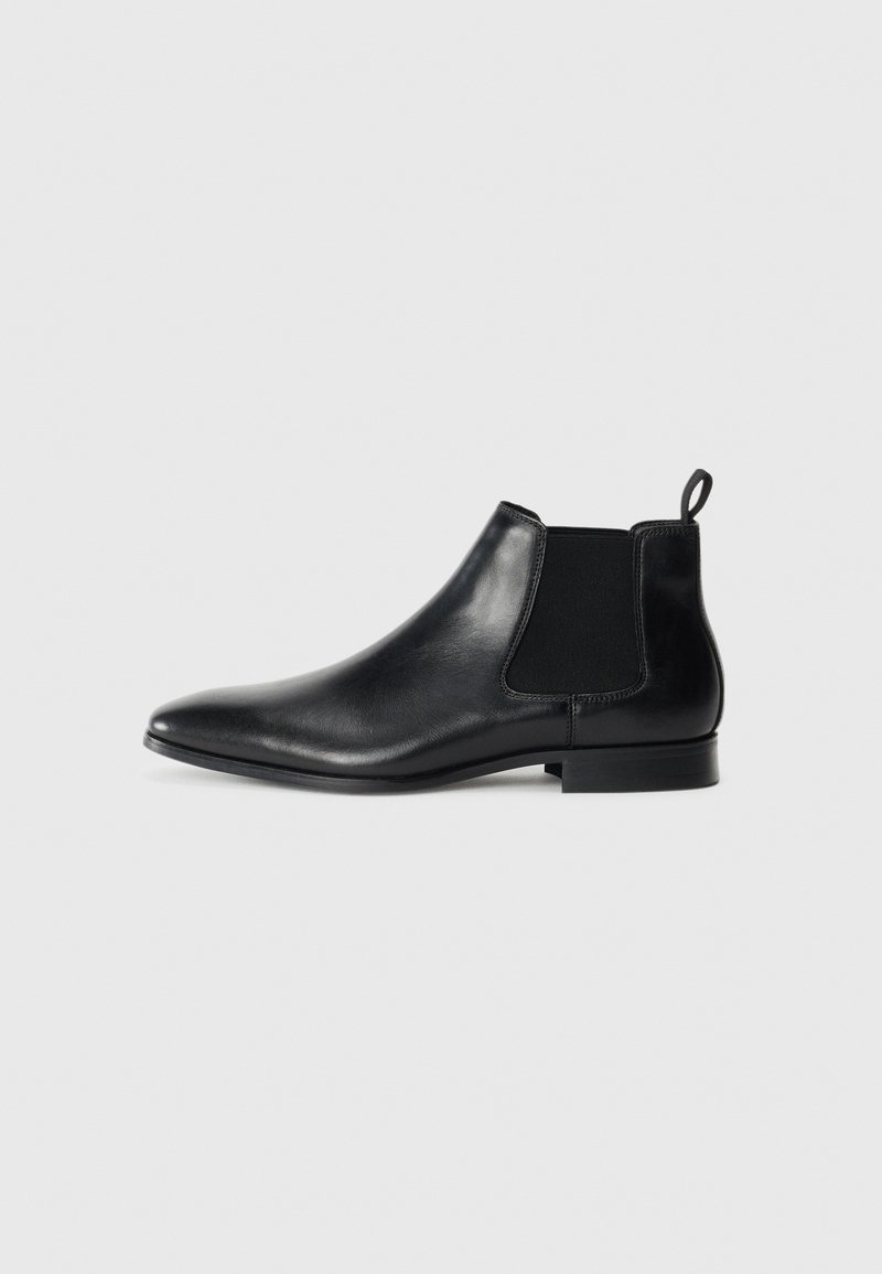 Botas de tobillo de cuero negro con paneles elásticos en los lados, puntera afilada y un pequeño tacón. Presenta una lengüeta en la parte posterior para facilitar su uso.