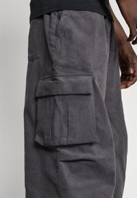 Šedé manšestrové kalhoty s kapsami po stranách a texturovaným povrchem, zobrazené na neutrálním pozadí.