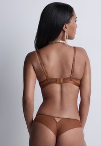 Ensemble de lingerie marron avec une texture lisse. Le soutien-gorge présente des bretelles réglables et une fermeture à crochet, tandis que les culottes arbore un détail découpé.