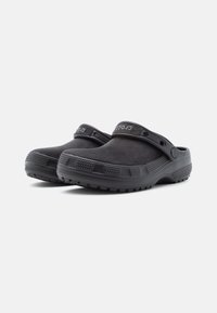 Pair of black slip-on clogs with textured soles and adjustable back straps, positioned on a white background.