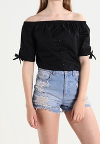 Top nero off-the-shoulder con maniche corte a sbuffo; presenta bottoni sulla parte frontale. Abbinato a pantaloni corti in denim azzurro chiaro con effetto usurato.