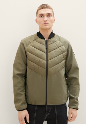 Ελαιόχρωμο bomber jacket με καπιτονέ σχέδιο σε σχήμα βέλους, μαύρο γιακά και κλείσιμο με φερμουάρ. Διαθέτει ελαφρώς γυαλιστερή υφή και ελαστικές μανσέτες.