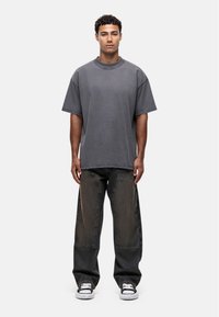 Szara bawełniana koszulka oversize z okrągłym dekoltem, zestawiona z ciemnymi, luźnymi dżinsami oraz białymi sneakersami. Widok z przodu.