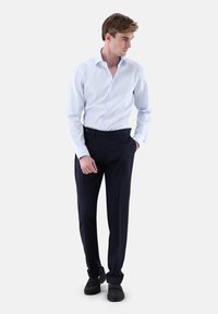 Hellblaues Hemd mit Knopfleiste, strukturiertem Kragen und langen Ärmeln, kombiniert mit dunkelblauen, maßgeschneiderten Hosen und schwarzen Schuhen.