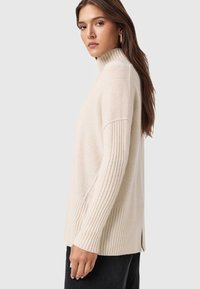 Jasnoszary sweter z golfem o ribbowym wzorze, z bocznymi rozporkami i luźnym krojem. Miękki materiał z długimi rękawami i lekko oversize'owym fasonem.