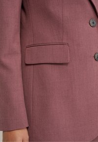 Mörkröd skräddarsydd kavaj med en bröstficka, rundade slag och två knappknäppningar, tillverkad av ett strukturerat tyg.