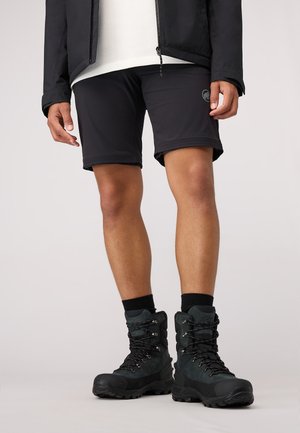 Zwarte shorts met een slim fit, gecombineerd met robuuste zwarte wandelschoenen met veters en gestructureerde zolen, tegen een neutrale achtergrond.