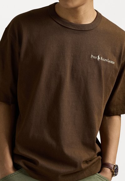 Brahna bomba T-shirt z rebrastim ovratnikom, ki ima majhen bel logo "Polo Ralph Lauren" na levem prsnem predelu. Kratke rokave.