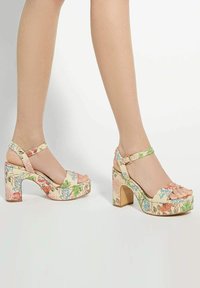 Sandales plateforme florales avec un talon épais et une sangle de cheville. Le tissu présente des fleurs multicolores sur un fond clair. Design à bout ouvert.