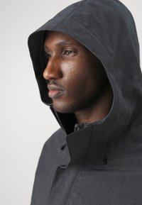 Dark gray waterproof jacket with a fitted hood, textured fabric, high collar, and zipper closure. Minimalistic design, no visible patterns.