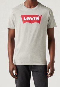 Camiseta de algodón gris con un gran logo rojo de "Levi's" en el frente, mangas cortas y un diseño clásico de cuello redondo.