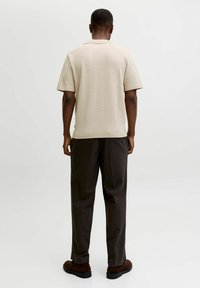 Chemise beige à manches courtes avec une texture en maille structurée, associée à un pantalon marron foncé, ample. La tenue présente une coupe droite.