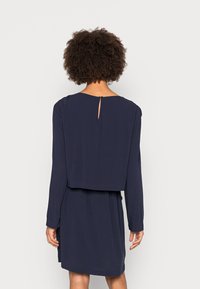 Vestido azul marino con mangas largas, escote redondeado y cierre de botón en el escote de la espalda; tejido suave y ligero, corte a la altura de la rodilla.