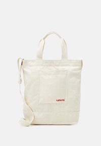 Torba typu tote z płótna w kolorze off-white z przednią kieszenią, górnymi uchwytami i regulowanym paskiem na ramię. Zawiera czerwone logo "Levi's".