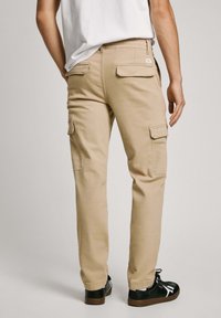 Khaki cargo nohavice so striedmym strihom, s dvoma vreckami na klopu na stehnách a hladkým zadným dílem. Nosí sa s čiernymi šnurovacími teniskami.