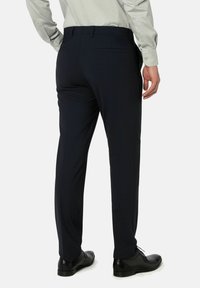 Marineblauwe broek gemaakt van textuurstof, met een slim fit, riemlussen en twee achterzakken. Ggedragen met zwarte dress schoenen.