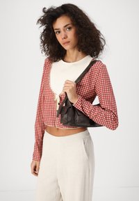 Camisa corta de cuadros roja y blanca con un cuello crema, combinada con pantalones anchos beige claros y un pequeño bolso marrón oscuro.