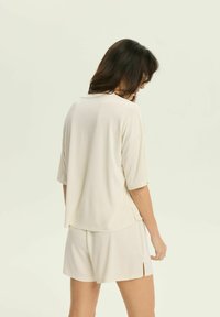 Cream-colored loose-fitting t-shirt with short sleeves and side slits, paired with matching shorts. Soft fabric with minimal texture.