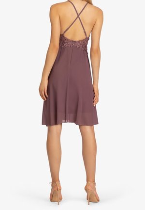 Robe en chiffon violet avec un corsage en dentelle florale, des bretelles croisées ajustables et un ourlet évasé, associée à des chaussures à talons transparents.