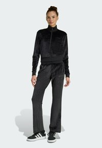 Černý sametový teplákový komplet s kab átkem na zip a odpovídajícími kalhotami. Obsahuje hladkou texturu, elastický pas a logo Adidas na hrudi.