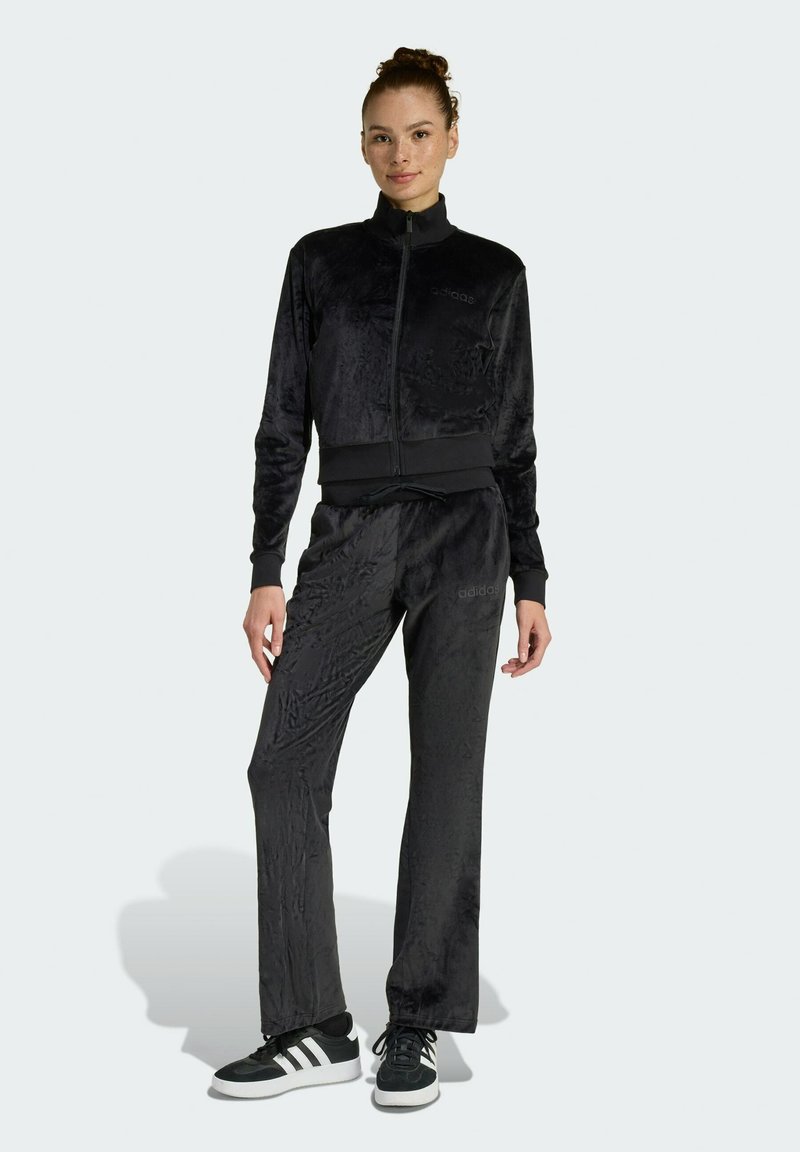 Černý sametový teplákový komplet s kabátkem na zip a odpovídajícími kalhotami. Obsahuje hladkou texturu, elastický pas a logo Adidas na hrudi.