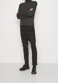 Zwarte geruite broeken met een trekkoord in de taille, gecombineerd met een donkergrijze coltrui en zwarte veterschoenen. Soepele textuur, slim fit.