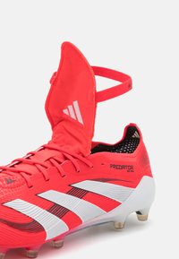 Rode voetbalschoenen met een gestructureerde bovenkant, witte streepaccenten en een scharnierende kraag. Voorzien van een gevoerde inlegzool en gevormde noppen voor grip.