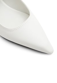 Vit läder platt sko med spetsig tå, med en slät yta och minimal sömnadsdetalj längs öppningen, med en svart sula.