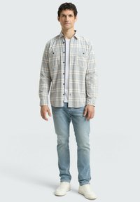 Licht geruit overhemd met lange mouwen, twee borstzakken, knoopsluiting, gedragen over een wit t-shirt en gecombineerd met lichtblauwe jeans en witte schoenen.