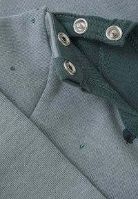 Bomullsskjorta i en mjuk blågrön nyans, med en ribbad krage som har silvriga tryckknappar och ett subtilt prickigt mönster.