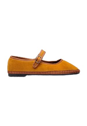 Zapato tipo Mary Jane plano de ante amarillo mostaza con ribete marrón, suela cosida, suela exterior negra y correa ajustable con hebilla redonda.