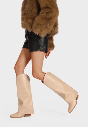 Beige laarzen tot over de knie met een zachte lederen textuur, hoekig ontwerp en een korte, gestapelde hak. Glad oppervlak en brede opening aan de bovenkant.