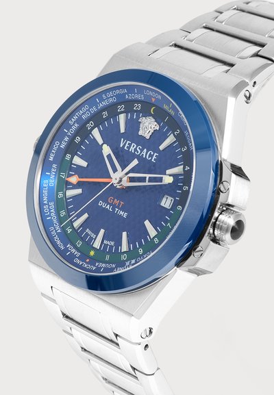 Ρολόι Versace GMT με διπλή ζώνη ώρας, μπλε καντράν, ασημένιο μπρασελέ, ζώνες ώρας πόλεων στην στεφάνη, ένδειξη ημερομηνίας και ασημί και πορτοκαλί δείκτες.