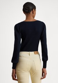 Tmavomodrý rebrovaný sveter s dlhými nafúknutými rukávmi a širokým výstrihom, skombinovaný s krémovými priliehavými nohavicami s logom na zadnej strane.