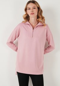 Felpa rosa con zip parziale frontale, texture a costine, maniche lunghe e fessure laterali; vestibilità rilassata. Ideale per abbigliamento casual o come strato aggiuntivo.