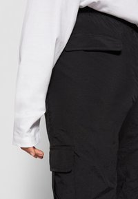 Svarta cargobyxor med texturerad yta, med en sidficka och avslappnad passform, kombinerade med en vit långärmad skjorta.