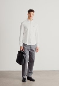 Biela košeľa na gombíky, sivé nohavice, čierna taška. Hladká látka, ušitý dizajn, minimalistický štýl bez vzorov. Čierne kožené topánky.