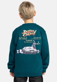 Teal sweatshirt med en stor grafik av en skateboardåkares på en bil, med texten "DC Shoe Company" och ytterligare designelement i flera färger.