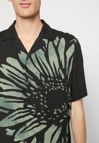 Czarny t-shirt z krótkim rękawem, z dużym zielonym wzorem kwiatowym, z zapięciem na guziki z przodu, luźnym kołnierzykiem i gładką strukturą.