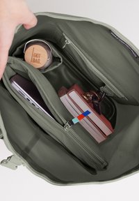 Oliivivihreä laukku, jossa on vetoketju, sisältää ruostumattomasta teräksestä valmistetun vesipullon, kannettavan tietokoneen, kirjoja ja avaimenperän, jossa on värikäs vetoketjun veto.