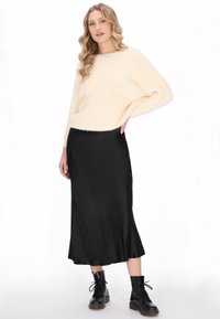 Crème gebreide trui met een ontspannen pasvorm, zwarte satin midi rok en zwarte combat boots. De outfit heeft zachte texturen en een eenvoudig ontwerp.