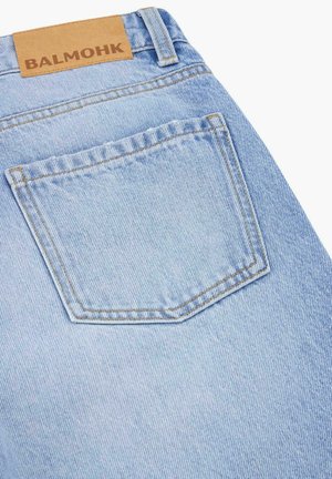 Jasnoniebieskie jeansy z denimu, zbliżenie pokazujące tylną kieszeń oraz brązową skórzaną metkę z napisem „BALMOHK”.