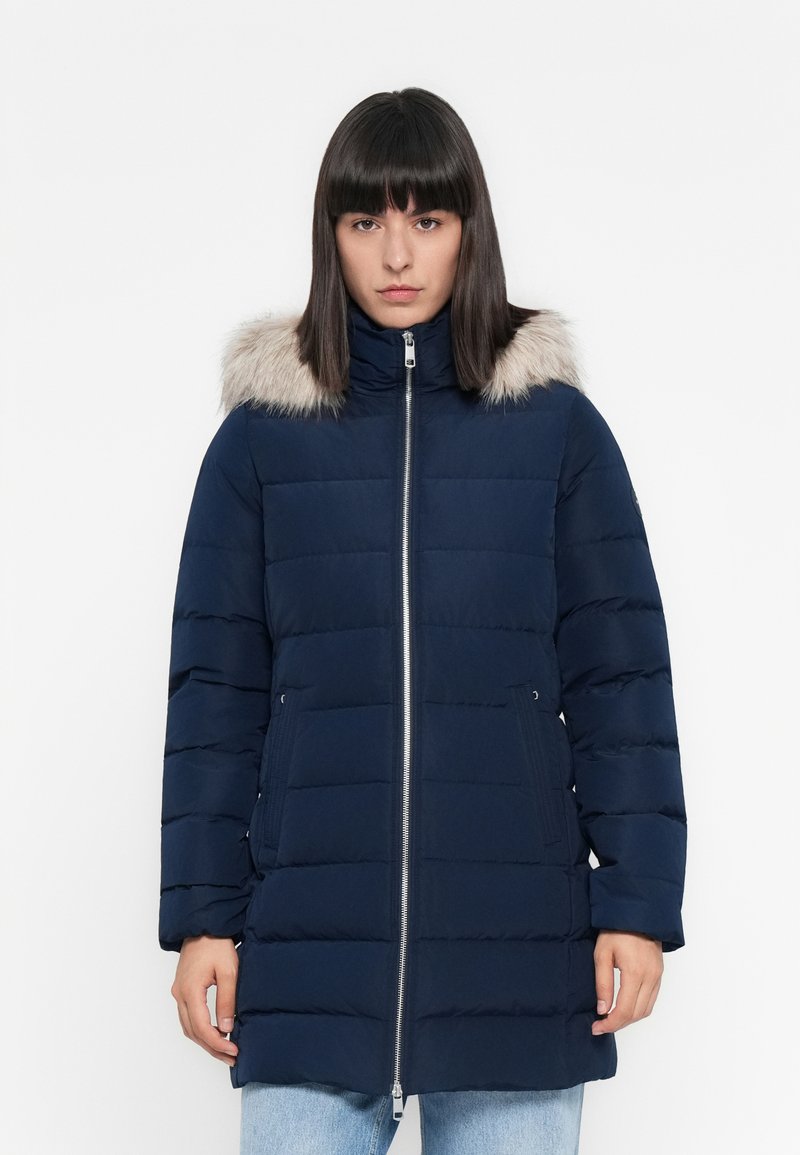 Giubbotto piumino blu navy con cappuccio foderato in pelliccia, dotato di zip frontale, design trapuntato, due tasche laterali e un taglio di lunghezza media.
