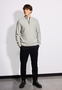 Světlé šedé pulovrové tričko s žebrovanou strukturou a límcem na půl zip, v kombinaci s černými slim-fit kalhotami a černými kotníkovými botami. Hladká textura.